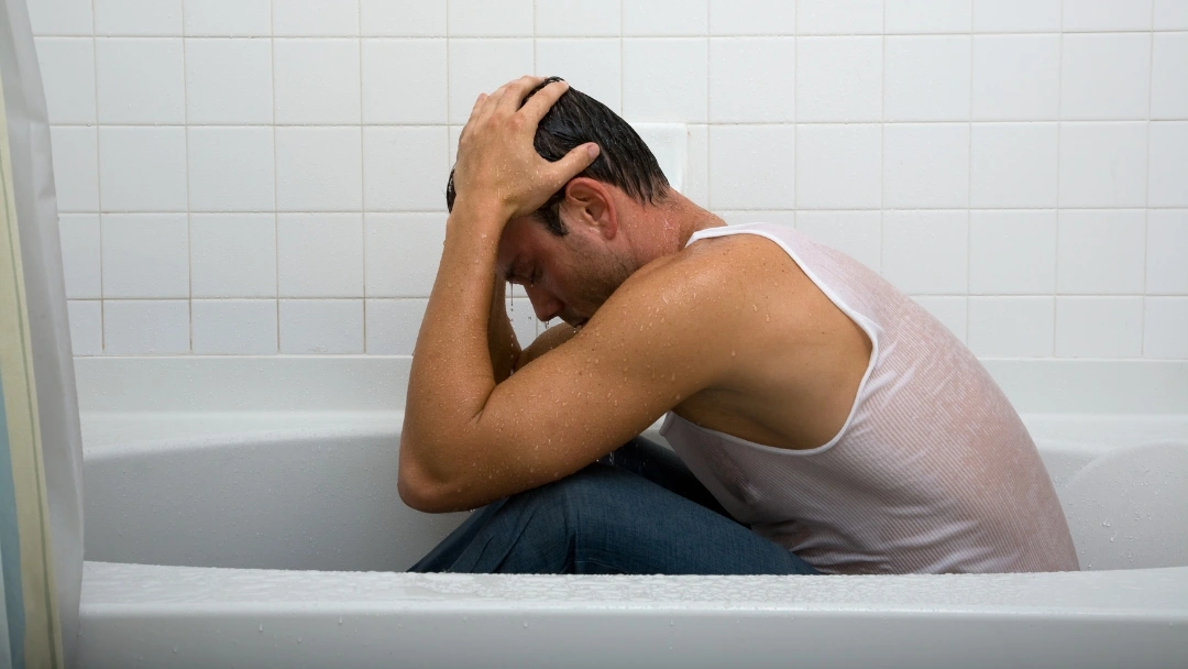 Person sitting on a shower stool under a handheld showerhead with lukewarm water